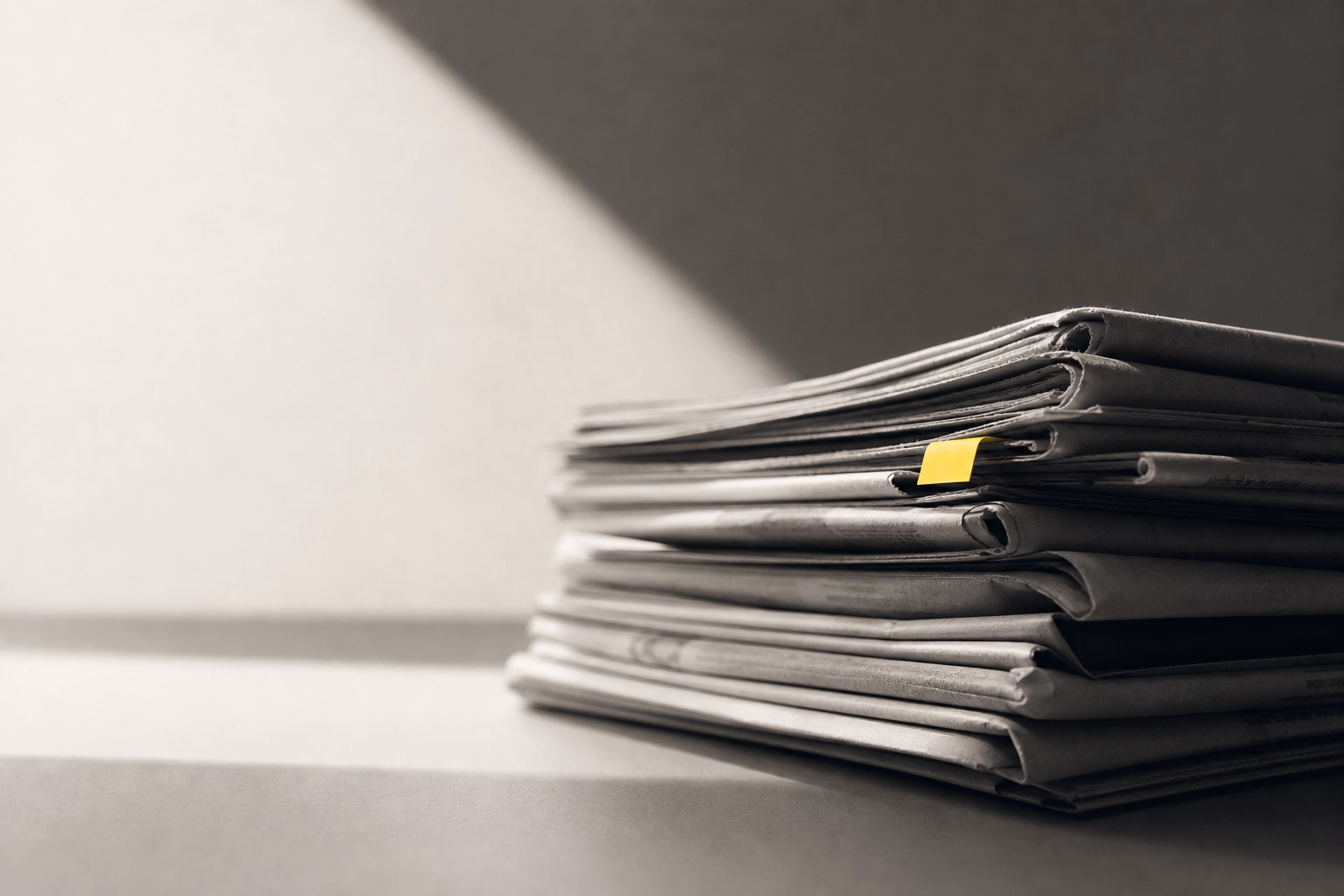 Newspaper, laptop and pen arranged on a desk beside printed business notes and a cup of coffee