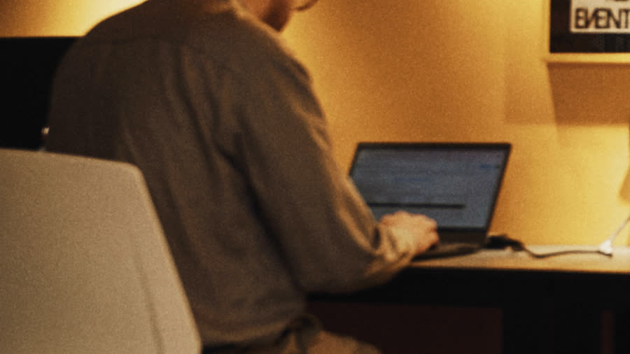 A Rostrum writer typing at a laptop by the yellow wall