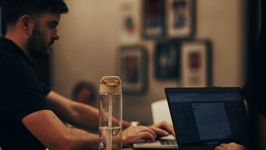 A Rostrum designer at his laptop, framed posters on the wall behind him