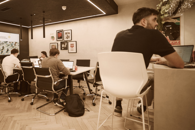 Four people work at desks in a modern office, with framed artwork, computers and pendant lights